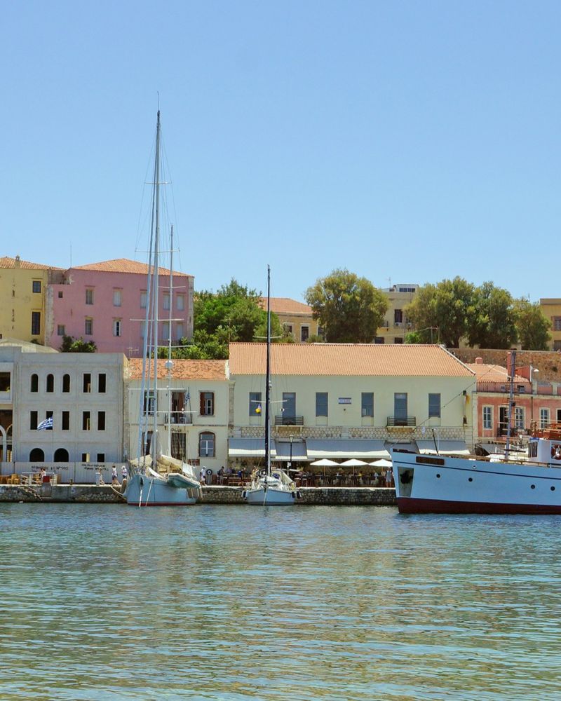 Venezianischer Hafen von Chania auf Kreta mit Segelbooten, einem Ausflugsschiff und bunten Häusern am Kai