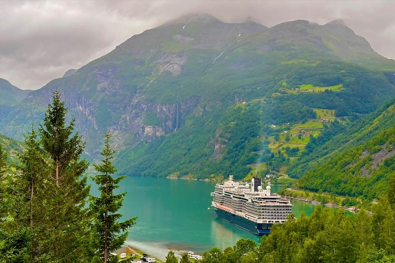 Kreuzfahrtschiff im Geirangerfjord in Norwegen zwischen steilen grünen Bergen unter tief hängenden Wolken